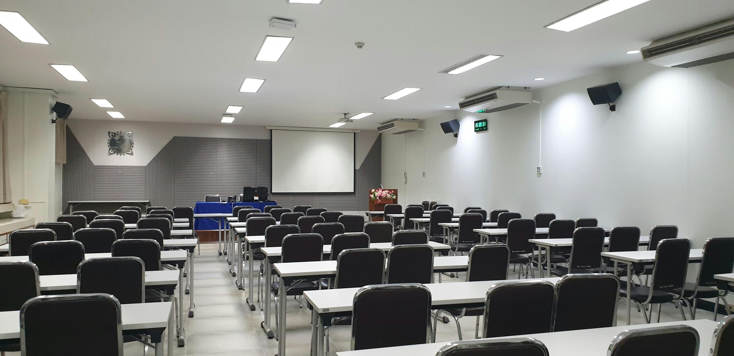Spacious empty conference room with neatly arranged tables and chairs, ready for a meeting or class.