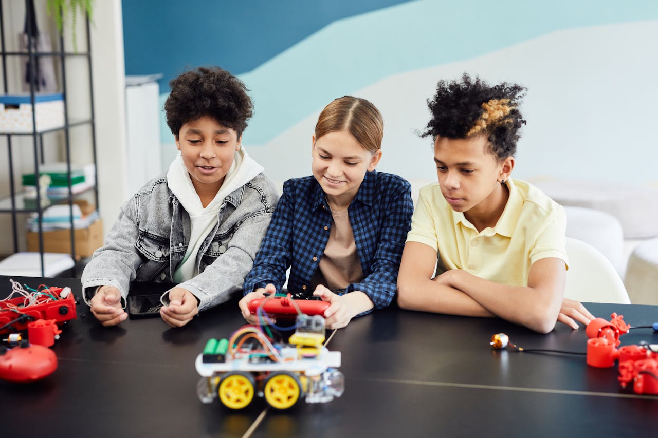 Teens exploring and building robotics at a table indoors, showcasing teamwork and technology skills.